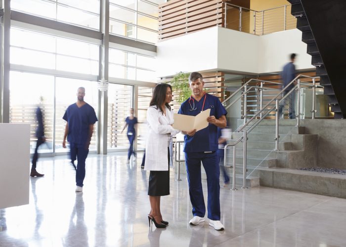 Two healthcare workers talk in the lobby of a busy hospital